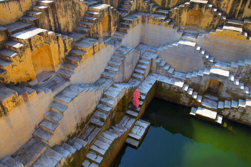 High angle view of woman wearing pink saris walking up stairwell around water pool of an ancient building. - MINF03933