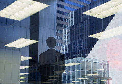 Rear view of man wearing suit standing at window, reflections of recessed office ceiling lights and skyscrapers. - MINF03934