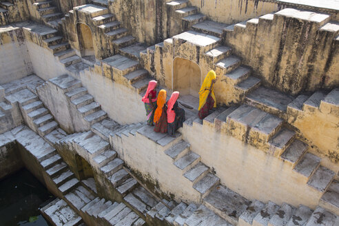 High angle view of four women wearing saris walking up stairwell around water pool of an ancient building. - MINF03936