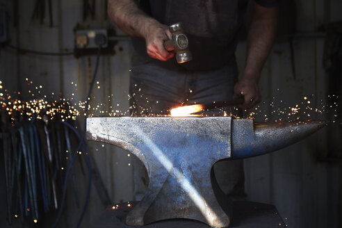 A blacksmith shaping a hot piece of iron on an anvil with a hammer, with sparks flying. - MINF03965