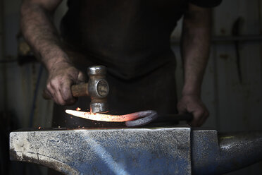 A blacksmith shaping a hot piece of iron on an anvil using a hammer. - MINF03967