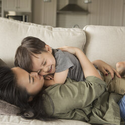 Eine Frau liegt auf einem Sofa, lächelt und kuschelt mit ihrem kleinen Sohn. - MINF03980