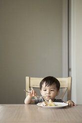 Young boy sitting on a chair at a table, eating a slice of cake. - MINF03981