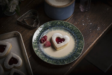 Backen zum Valentinstag, Blickwinkel auf einen Teller mit herzförmigen Keksen und frischen Himbeeren. - MINF03990