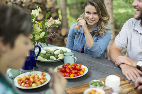 Three people seated at a table outdoors, with fresh fruit and vegetables in plates on the table. - MINF04060