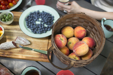 Blick von oben auf einen Picknicktisch mit einem Korb voller frischer Pfirsiche, einer Schale mit Blaubeeren und einem Salat zum Mittagessen im Freien. - MINF04066