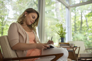 Eine sitzende Frau hält ein aufgeschlagenes Tagebuch und einen Stift in der Hand. - MINF04082