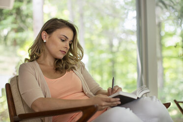 A woman seated holding an open journal and a pen. - MINF04083