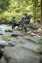 Two men seated in shade on the rocks by the river. - MINF04089