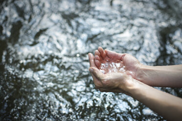 A man cupping his hands and scooping up clear water from a river. - MINF04094