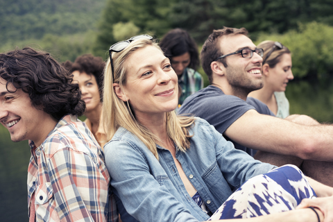 A group of women and men seated on a jetty by a lake in the countryside. stock photo