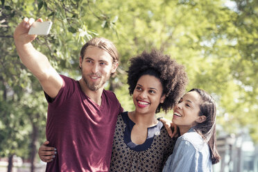 Three people, a man and two women, taking selfies in a city park - MINF04125