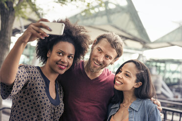 Drei Personen, ein Mann und zwei Frauen, machen Selfies im Park - MINF04126