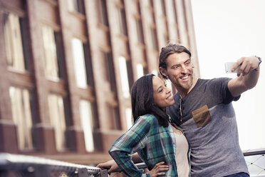 A couple, man and woman taking a selfie by a large building in the city - MINF04136