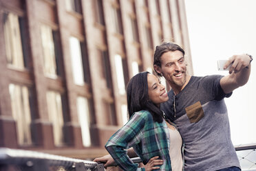 Ein Paar, Mann und Frau, machen ein Selfie vor einem großen Gebäude in der Stadt - MINF04136