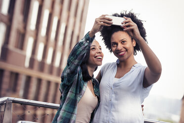 Two women posing and taking a selfie by a large building in the city - MINF04139