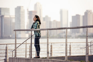 A woman standing on the waterfront, view to the city over the water in New York City. - MINF04143