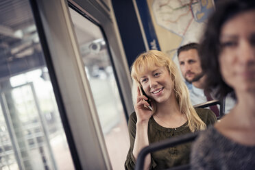 Eine blonde Frau in einem Stadtbus, die mit ihrem Smartphone telefoniert - MINF04146