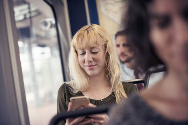 A blond woman on a bus looking down at her cell phone - MINF04147