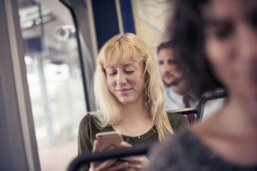 Eine blonde Frau in einem Bus, die auf ihr Handy schaut - MINF04147