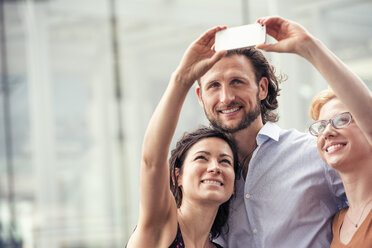 Ein Mann und zwei Frauen auf einer Straße in der Stadt, die ein Selfie mit einem Smartphone machen. - MINF04152