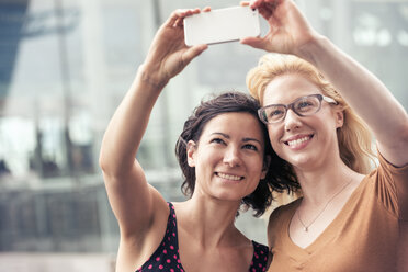 Zwei Frauen auf einer Straße in der Stadt, die ein Selfie mit einem Smartphone machen. - MINF04153