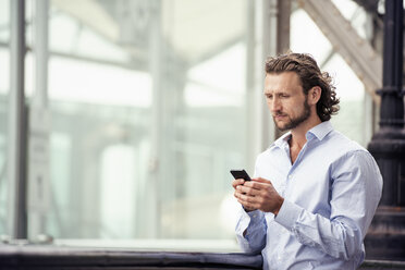 A man standing outdoors on the street, checking his cell phone. - MINF04156