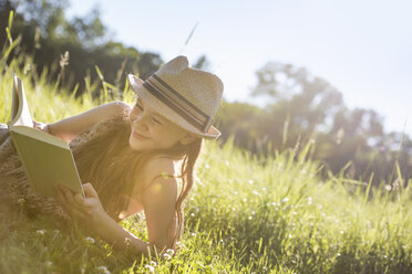 A young girl in a straw hat lying on the grass reading a book. - MINF04171