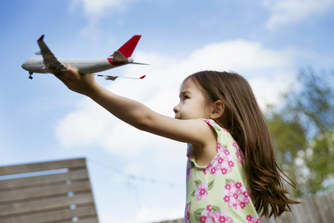 Junges Mädchen im Garten spielt mit Spielzeugflugzeug, lizenzfreies Stockfoto