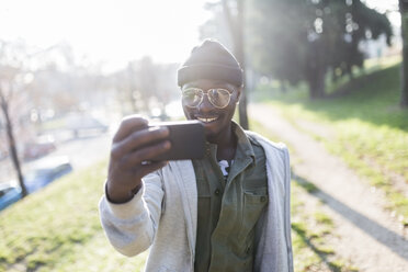 Junger Mann steht im Park und macht ein Selfie mit seinem Smartphone - GIOF04072