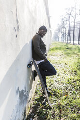 Cool young man leaning with skateboard on wall in in the city - GIOF04087