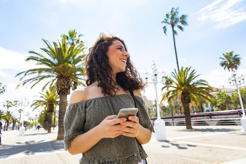 Lächelndes Teenager-Mädchen mit Smartphone an der Uferpromenade - WPEF00750