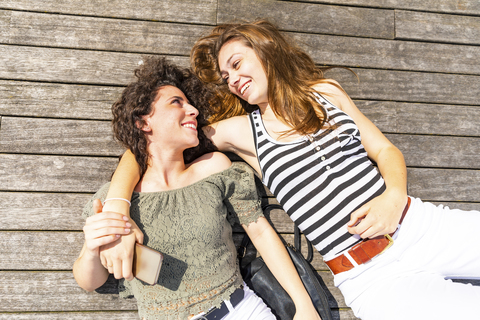 Zwei glückliche Freundinnen liegen auf einem Holzboden, lizenzfreies Stockfoto