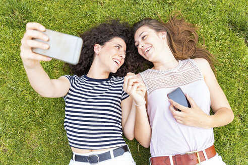 Zwei glückliche Freundinnen liegen im Gras und machen ein Selfie - WPEF00778