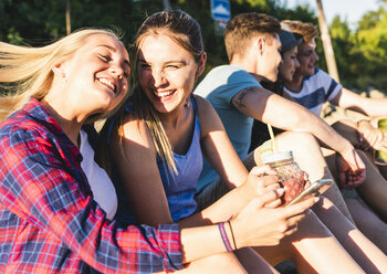 Gruppe glücklicher Freunde, die mit erfrischenden Getränken und Mobiltelefonen im Freien sitzen - UUF14810