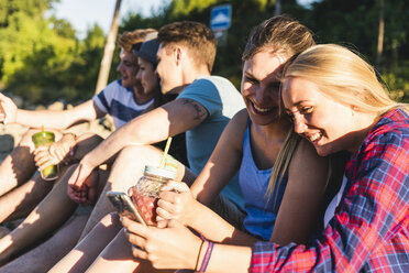 Gruppe glücklicher Freunde, die mit erfrischenden Getränken und Mobiltelefonen im Freien sitzen - UUF14811