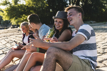 Eine Gruppe von Freunden sitzt mit Erfrischungsgetränken und Mobiltelefonen auf Kopfsteinpflaster - UUF14812