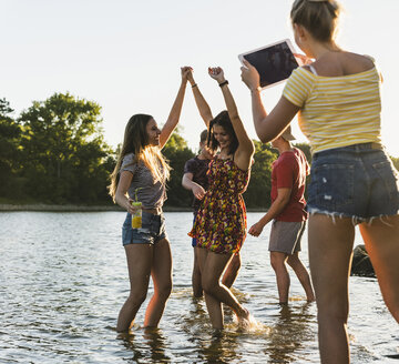 Gruppe von glücklichen Freunden mit Tablet in einem Fluss bei Sonnenuntergang - UUF14822