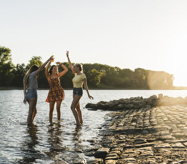 Drei glückliche junge Frauen in einem Fluss bei Sonnenuntergang - UUF14823