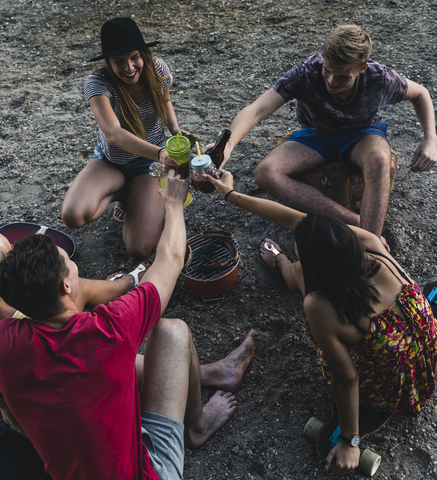 Eine Gruppe von Freunden sitzt zusammen, grillt und stößt an, lizenzfreies Stockfoto