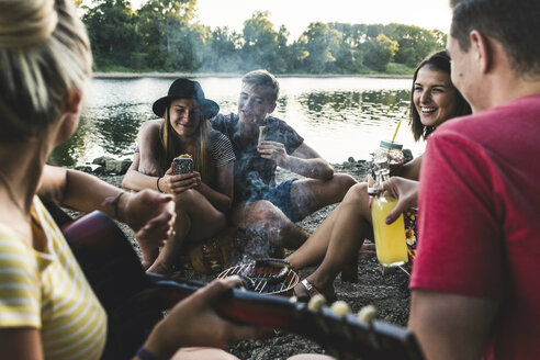 Eine Gruppe von Freunden sitzt beim Grillen am Flussufer zusammen - UUF14839
