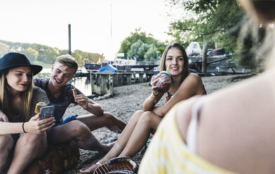 Eine Gruppe von Freunden sitzt beim Grillen am Flussufer zusammen - UUF14840