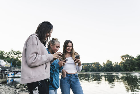 Drei junge Frauen benutzen Handys am Flussufer - UUF14842