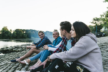 Group of friends sitting at the riverside in the evening - UUF14843