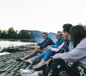 Group of friends sitting at the riverside in the evening - UUF14844