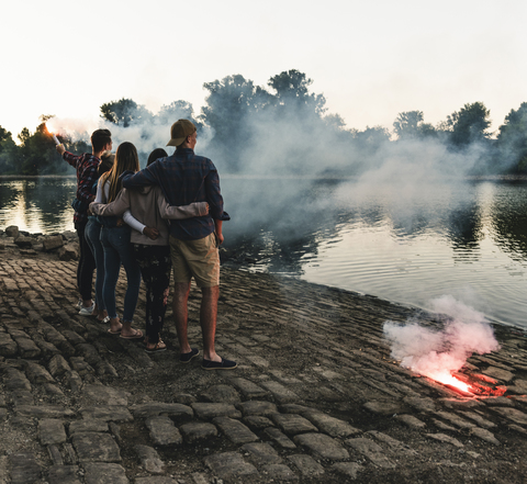 Group of friends standing at the riverside in the evening with torches stock photo