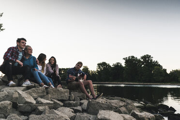 Group of friends sitting at the riverside in the evening - UUF14847
