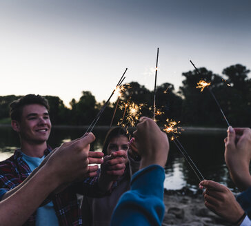 Gruppe von Freunden am Flussufer mit Wunderkerzen am Abend - UUF14848