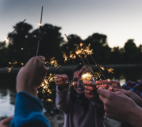 Gruppe von Freunden am Flussufer mit Wunderkerzen am Abend, lizenzfreies Stockfoto