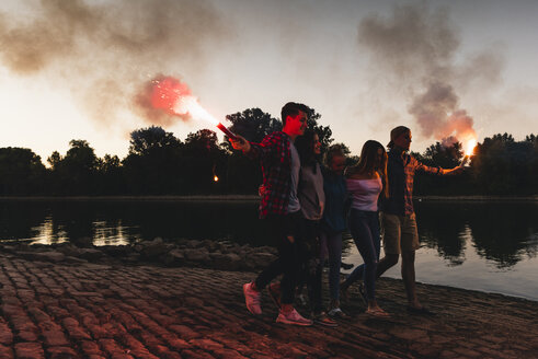 Gruppe von Freunden, die am Abend mit Fackeln am Flussufer spazieren gehen - UUF14854